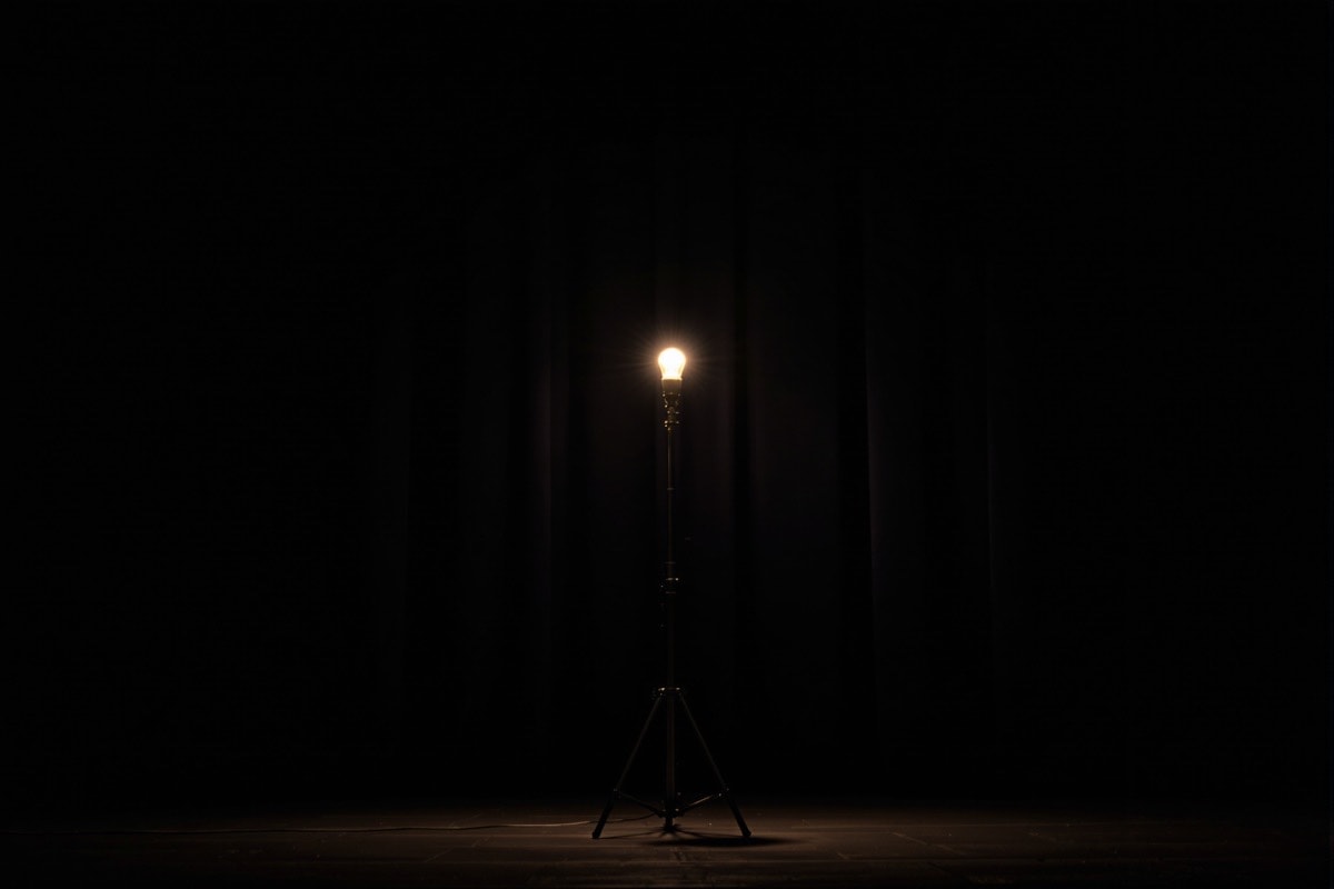 A single ghost light burning on an empty stage in front of a closed dark curtain