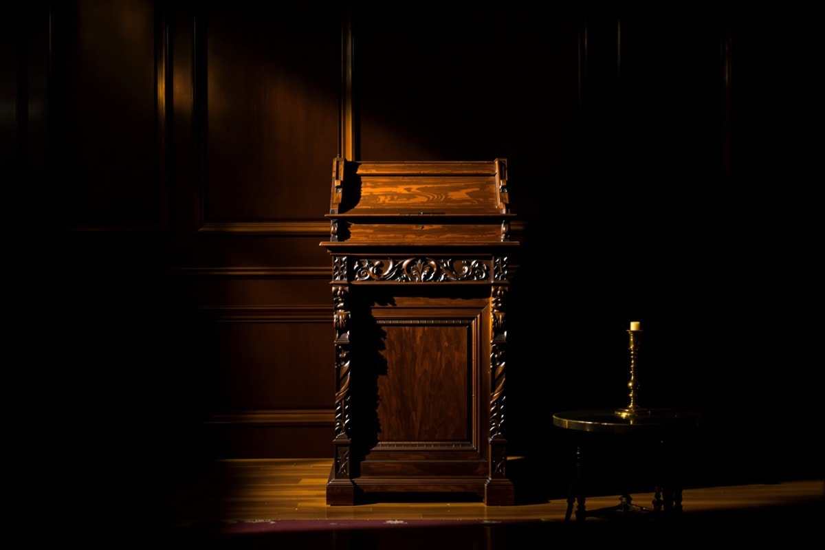 An antique carved wooden reading lectern standing empty in a pool of lamplight